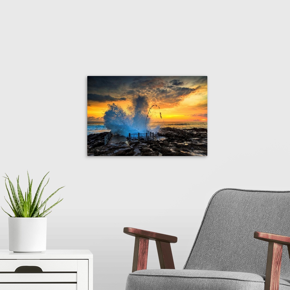 A modern room featuring Waves crashing onto the rocky shore at sunset.