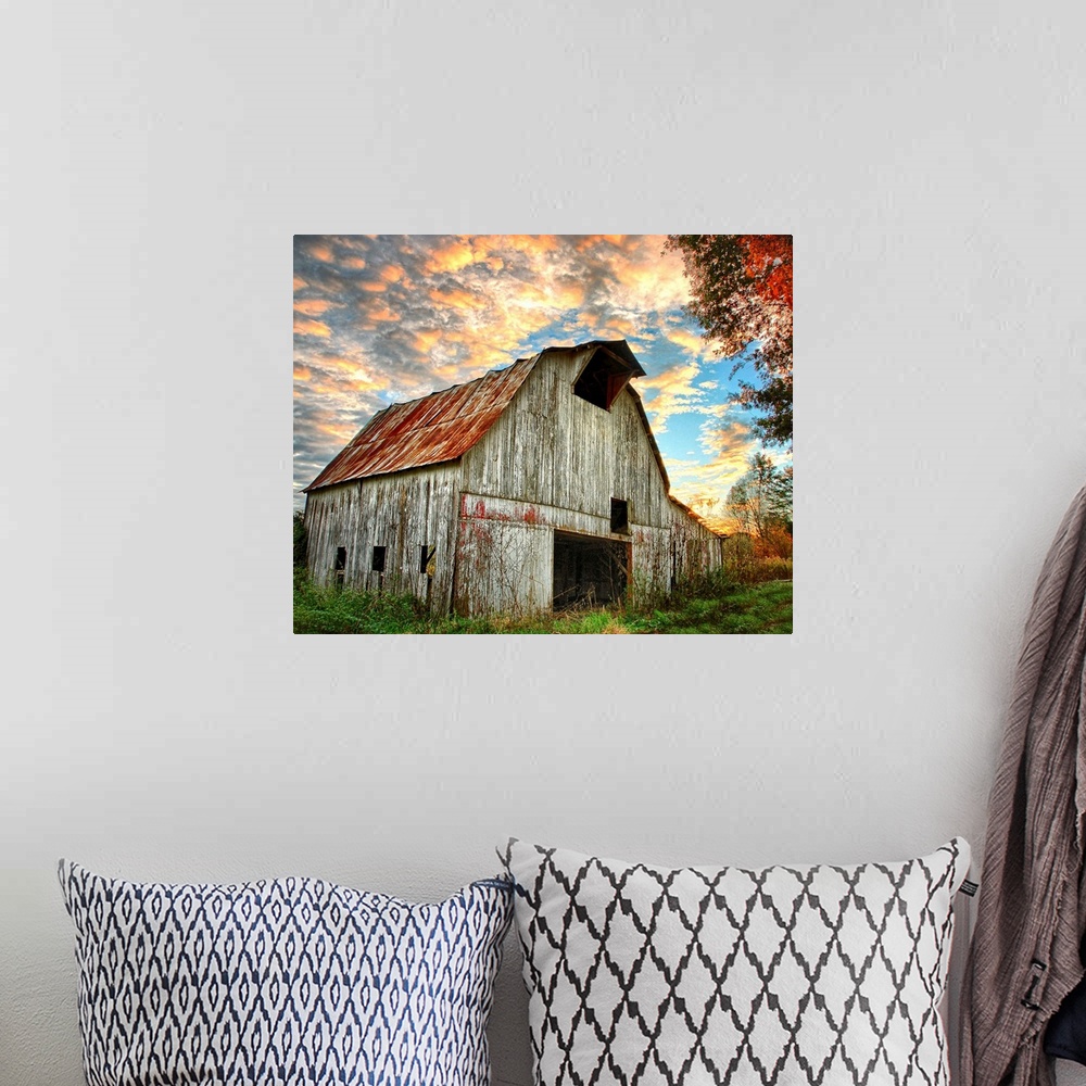 A bohemian room featuring Sunset over an old, weathered barn, with a cloudy sky.