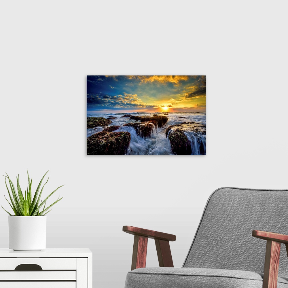 A modern room featuring Dramatic clouds of sunset hanging over a seascape with rocky shoreline in the foreground.