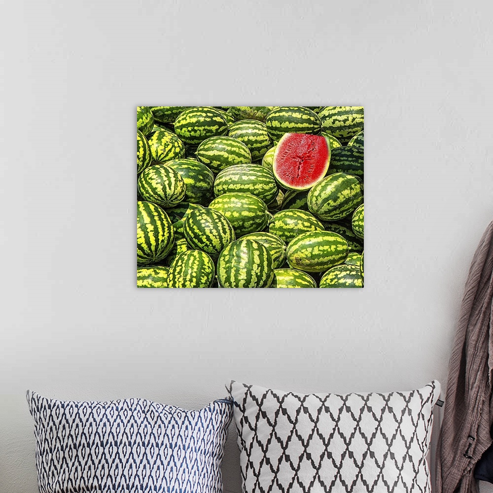 A bohemian room featuring A big bunch of watermelons with one sliced in half, revealing the red fruit.