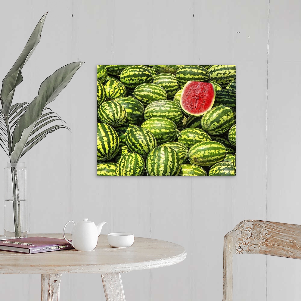 A farmhouse room featuring A big bunch of watermelons with one sliced in half, revealing the red fruit.