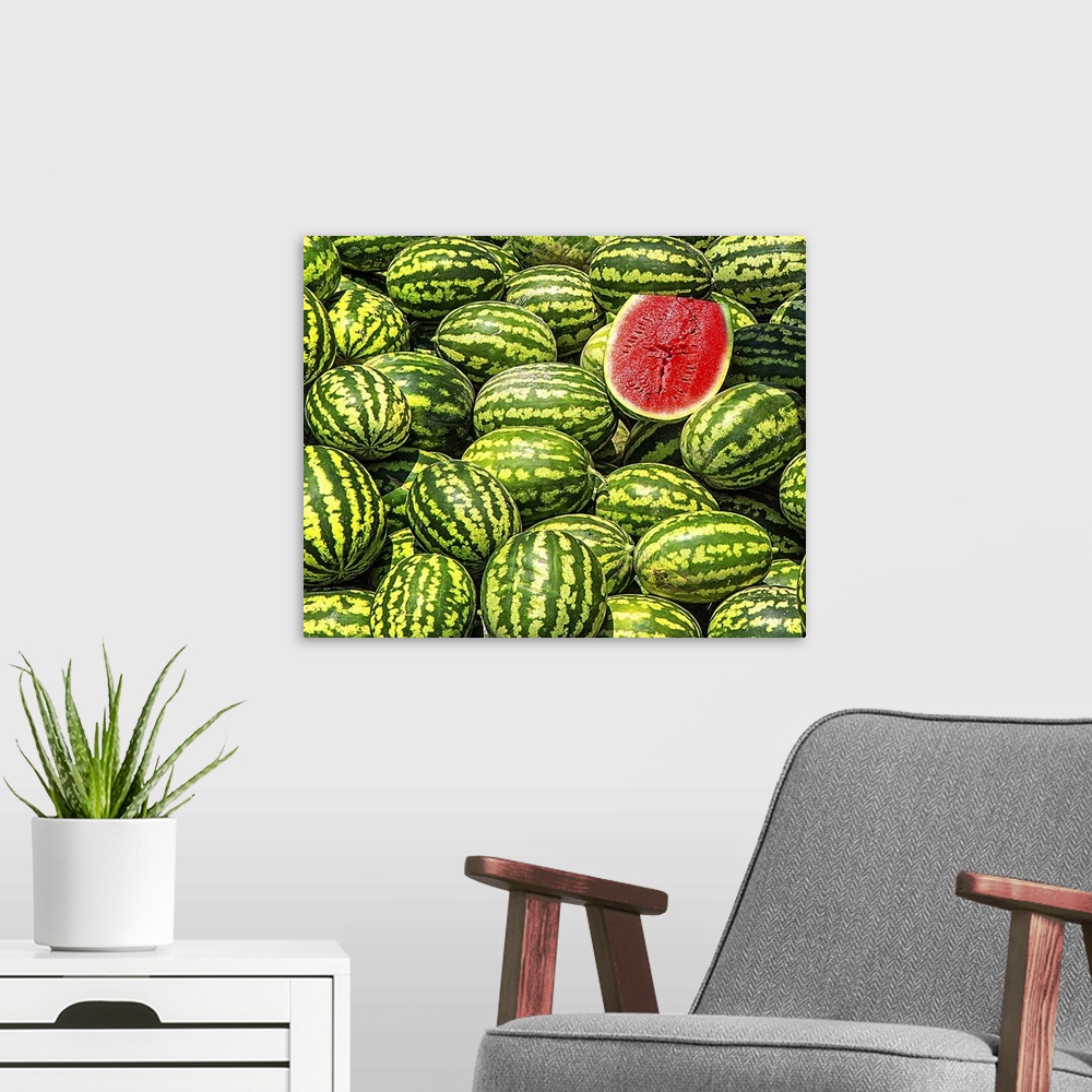 A modern room featuring A big bunch of watermelons with one sliced in half, revealing the red fruit.