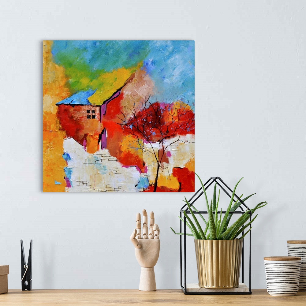 A bohemian room featuring A square abstract painting of a house with vibrant textured colors of red, yellow and blue.