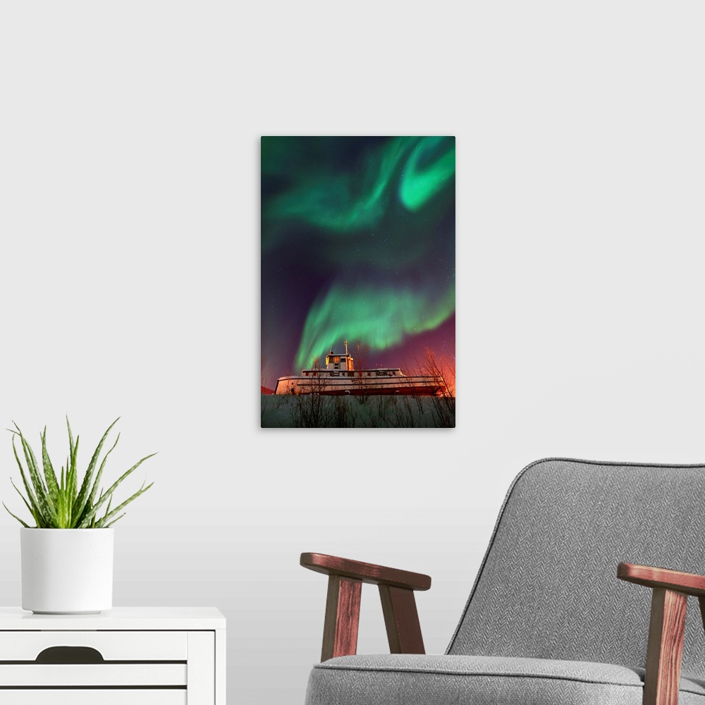 A modern room featuring Old steamboat under a sky full of dancing northern lights. Located in Dawson City, Yukon, Canada