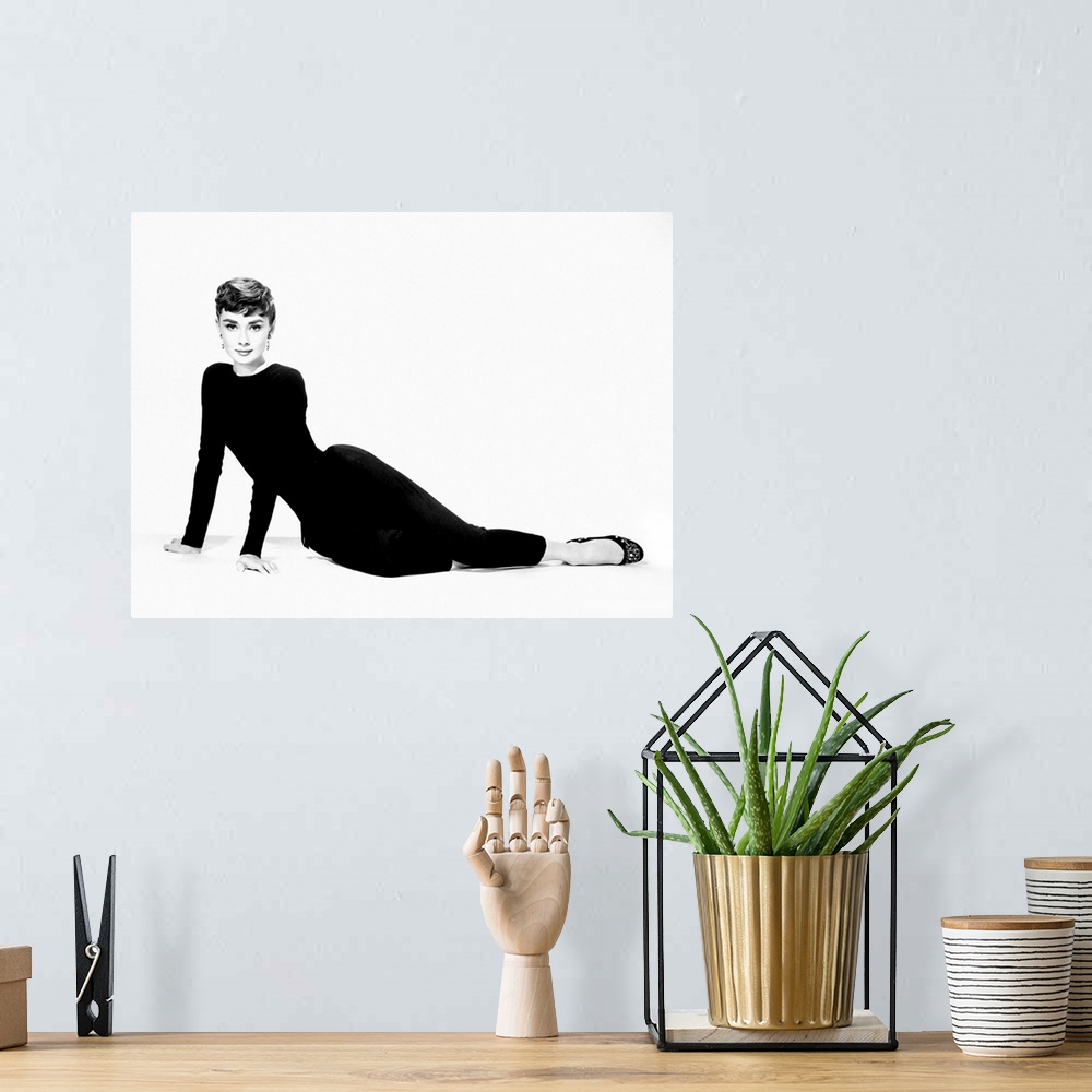 A bohemian room featuring A large piece of artwork in black and white of Audrey Hepburn sitting on her hip and both arms st...