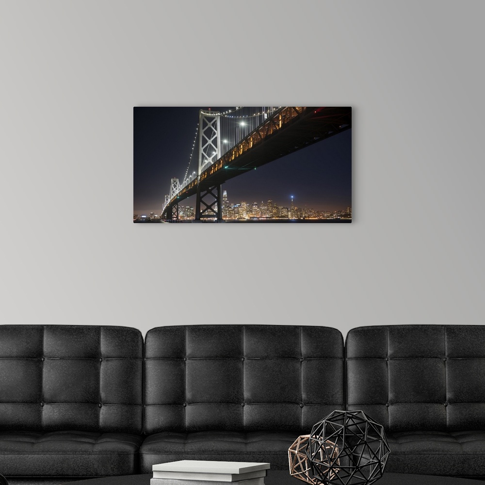 A modern room featuring Photograph of the Bay Bridge at night from below with the San Francisco skyline lit up in the bac...