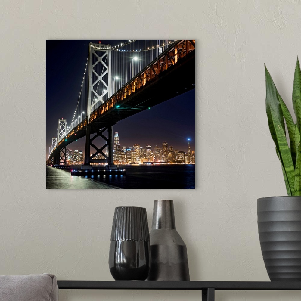 A modern room featuring Square photograph of the Bay Bridge lit up at night with the San Francisco skyline in the backgro...