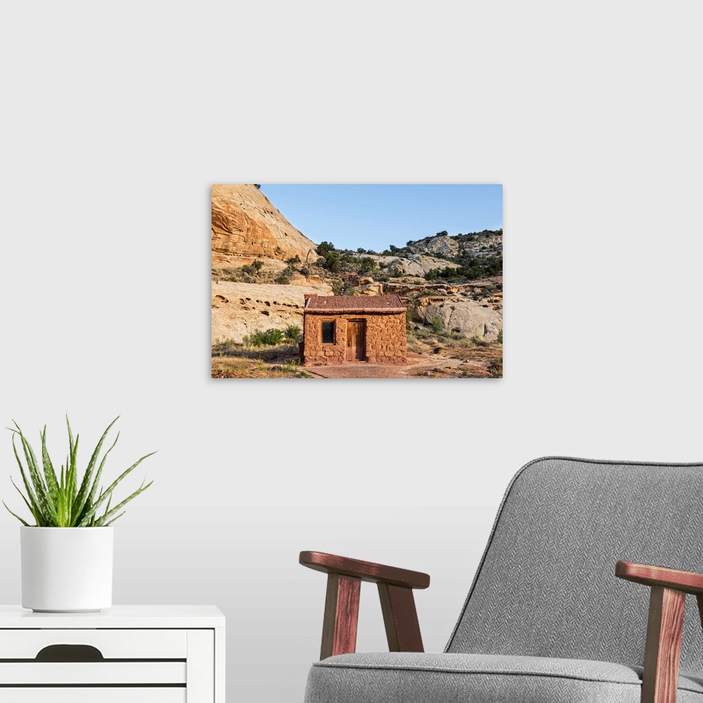 A modern room featuring Behunin Cabin with the cliffs of the Waterpocket Fold overlooking it at Capitol Reef National Par...