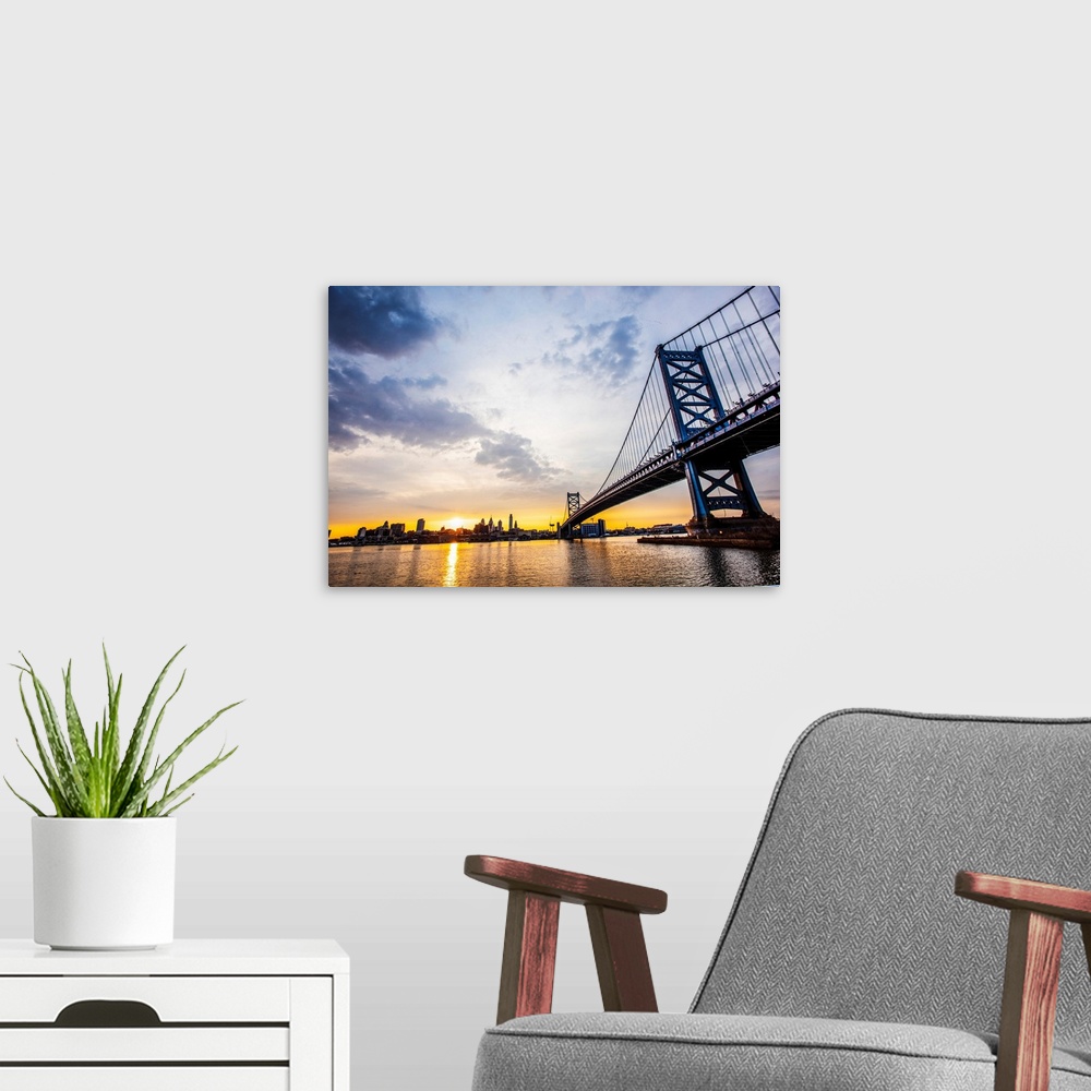 A modern room featuring The sun sets with dramatic clouds above Philadelphia's Ben Franklin Bridge.