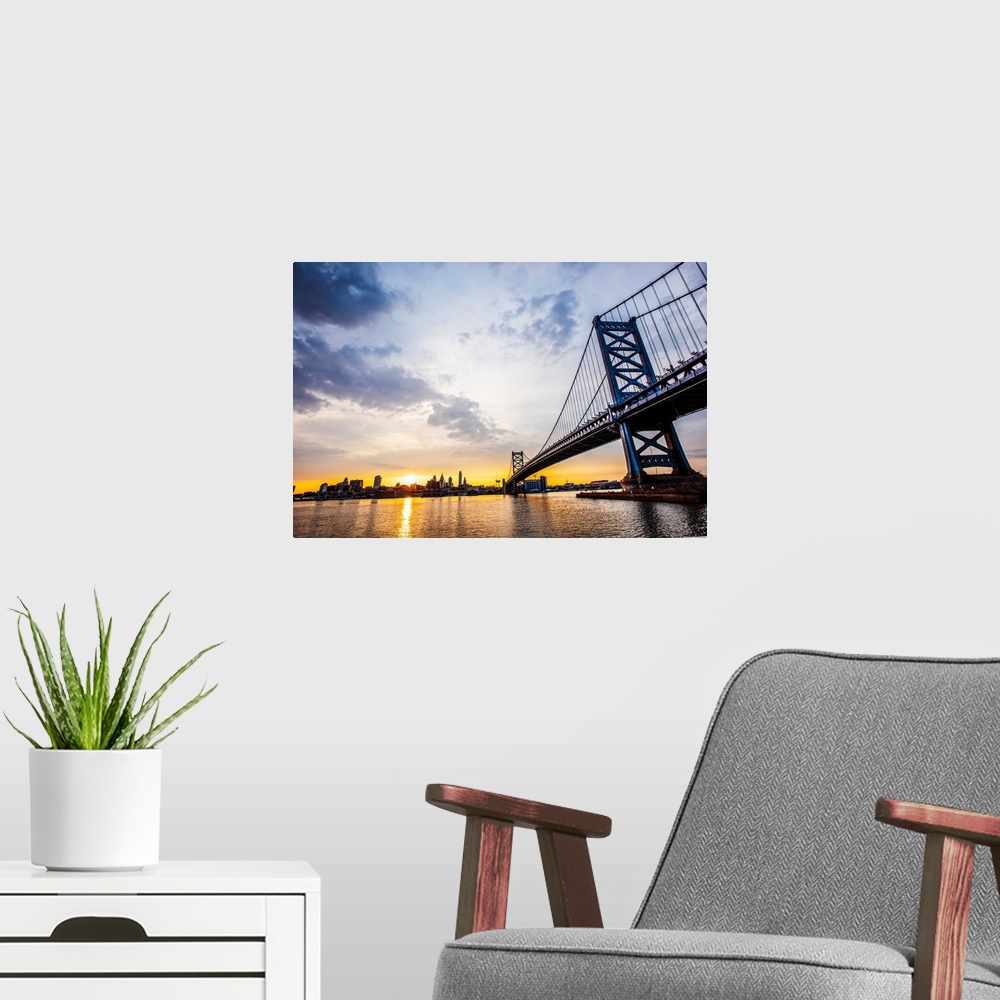 A modern room featuring The sun sets with dramatic clouds above Philadelphia's Ben Franklin Bridge.