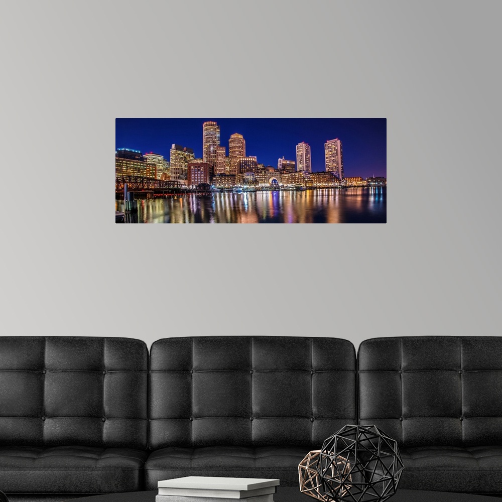 A modern room featuring Panoramic view of the Boston City skyline at night, with lights reflected in the water.