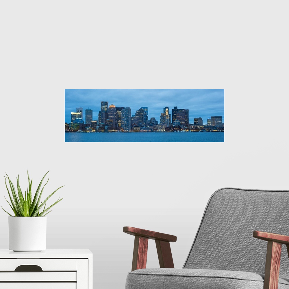 A modern room featuring Panoramic view of the Boston City skyline at night, with a cloudy sky overhead.