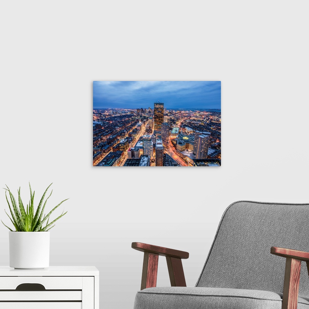 A modern room featuring View from a skyscraper of tall buildings in Boston glowing at night.