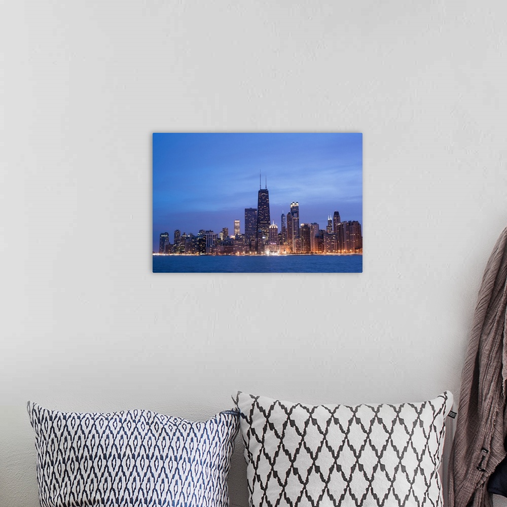 A bohemian room featuring The Chicago city skyline illuminated in the early evening, seen from across the water.