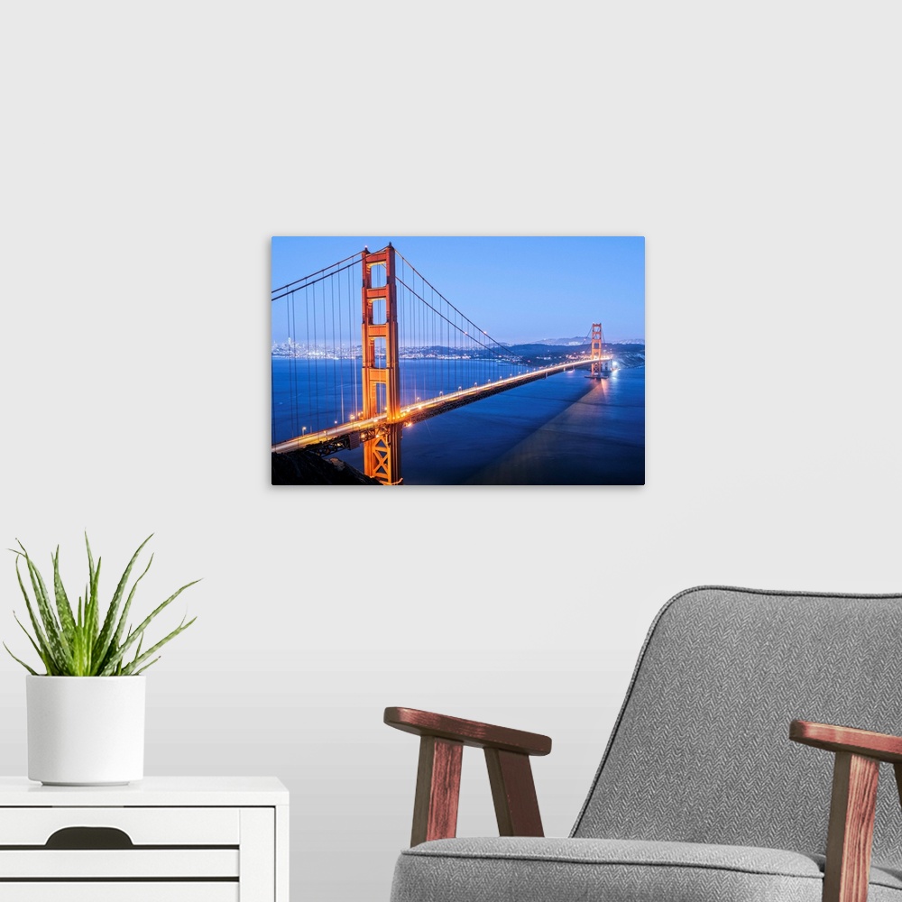 A modern room featuring Cool toned photograph of the Golden Gate Bridge lit up at twilight with the city lights in the ba...