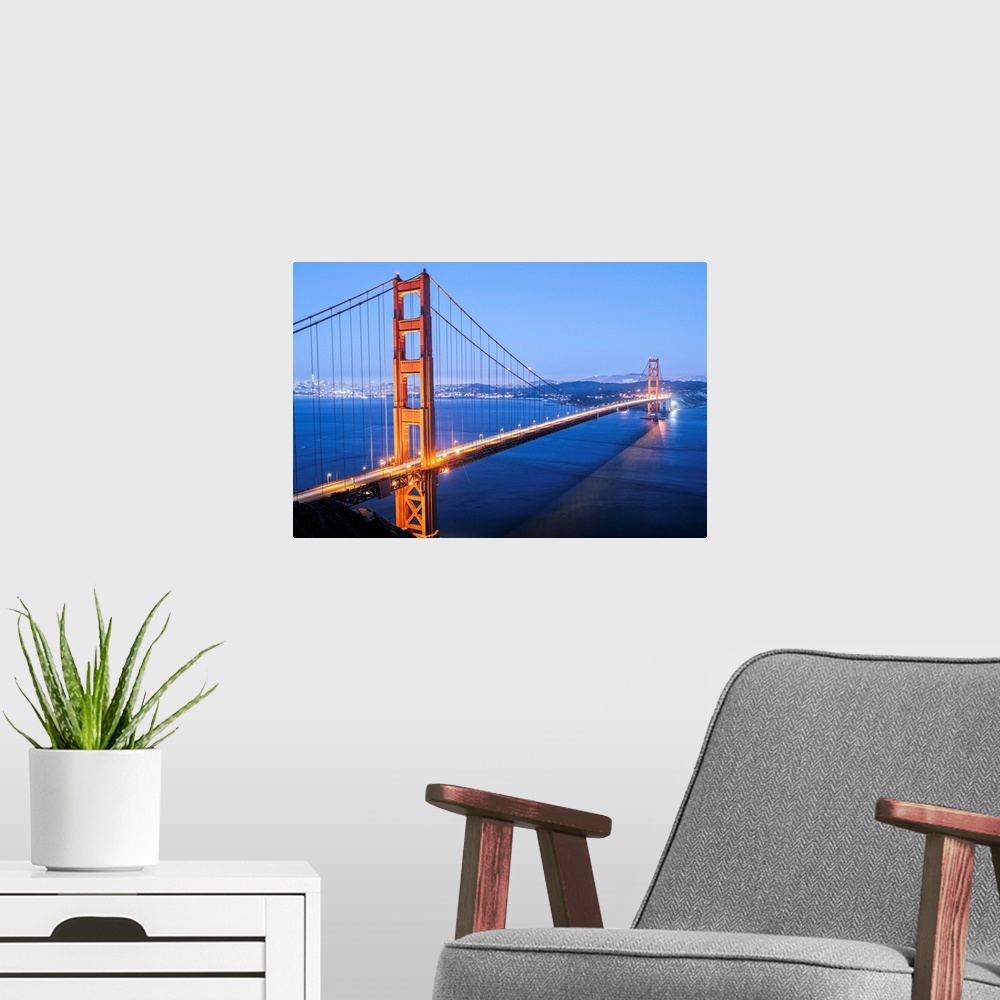 A modern room featuring Cool toned photograph of the Golden Gate Bridge lit up at twilight with the city lights in the ba...