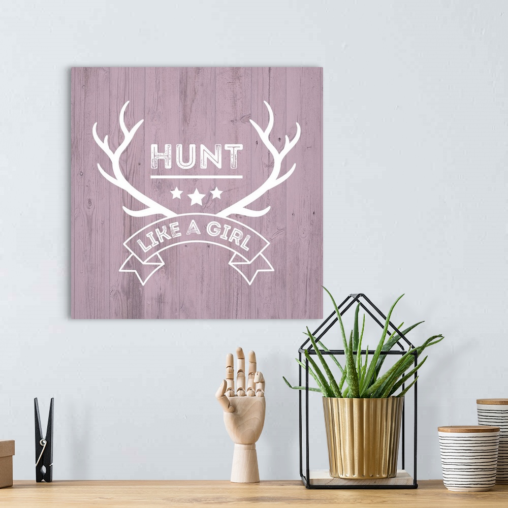 A bohemian room featuring Deer antlers and a banner reading "Hunt Like A Girl" on a distressed pink wood background.