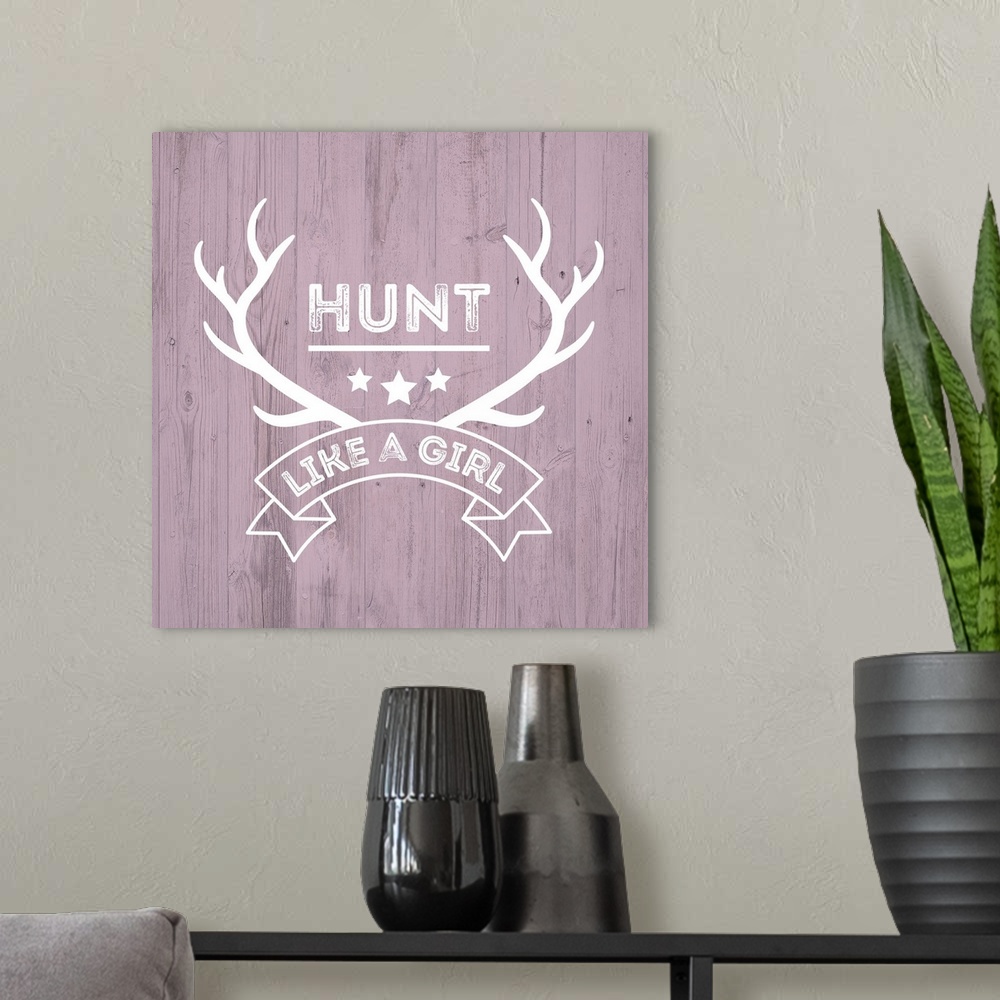 A modern room featuring Deer antlers and a banner reading "Hunt Like A Girl" on a distressed pink wood background.