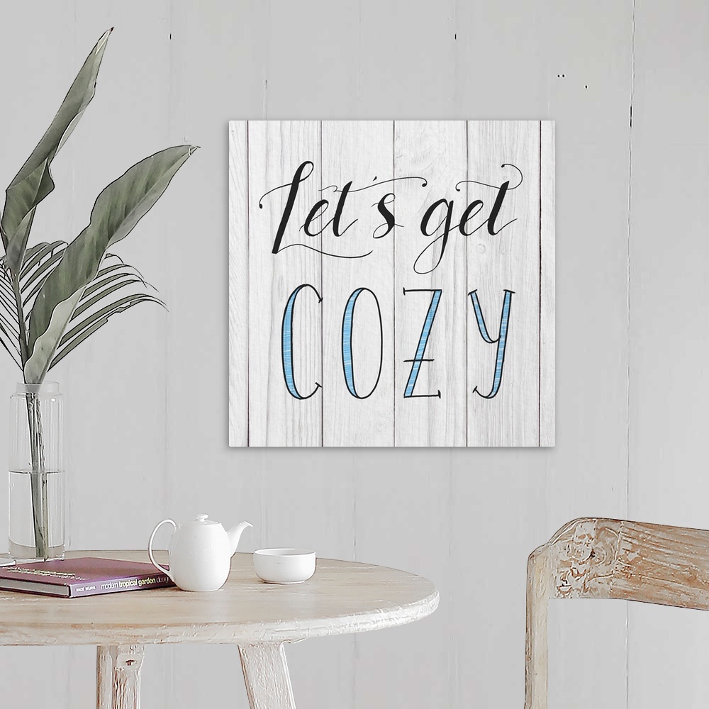 A farmhouse room featuring "Let's Get Cozy" handwritten in black and blue on a white wood panel background.