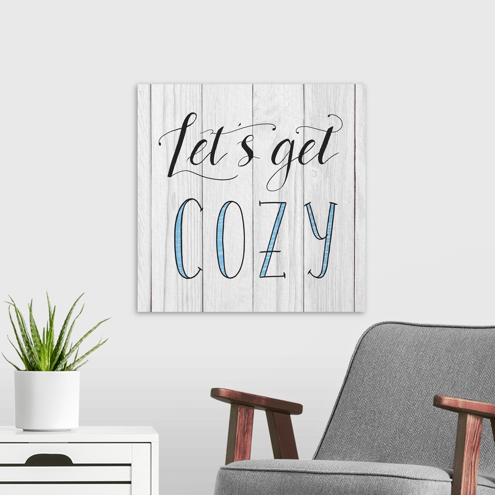A modern room featuring "Let's Get Cozy" handwritten in black and blue on a white wood panel background.