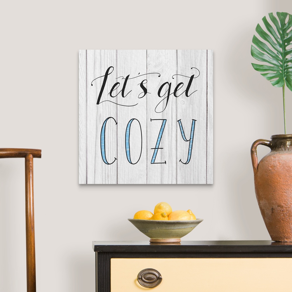 A traditional room featuring "Let's Get Cozy" handwritten in black and blue on a white wood panel background.