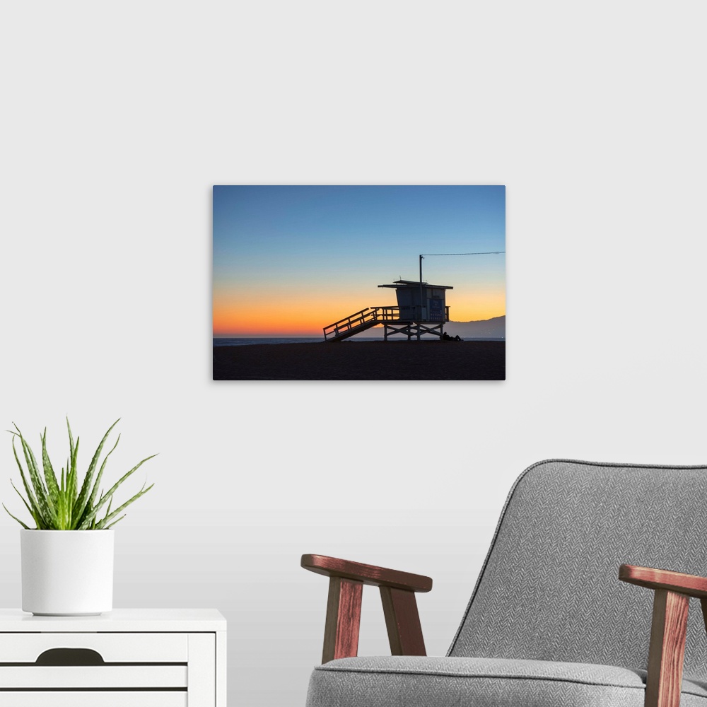 A modern room featuring The sun sets on Venice beach with the silhouette of a lifeguard tower.