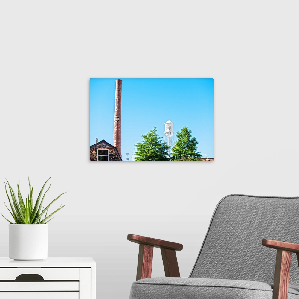 A modern room featuring Lucky Strike Water Tower and smokestack over the trees, with a blue sky behind, American Tobacco ...