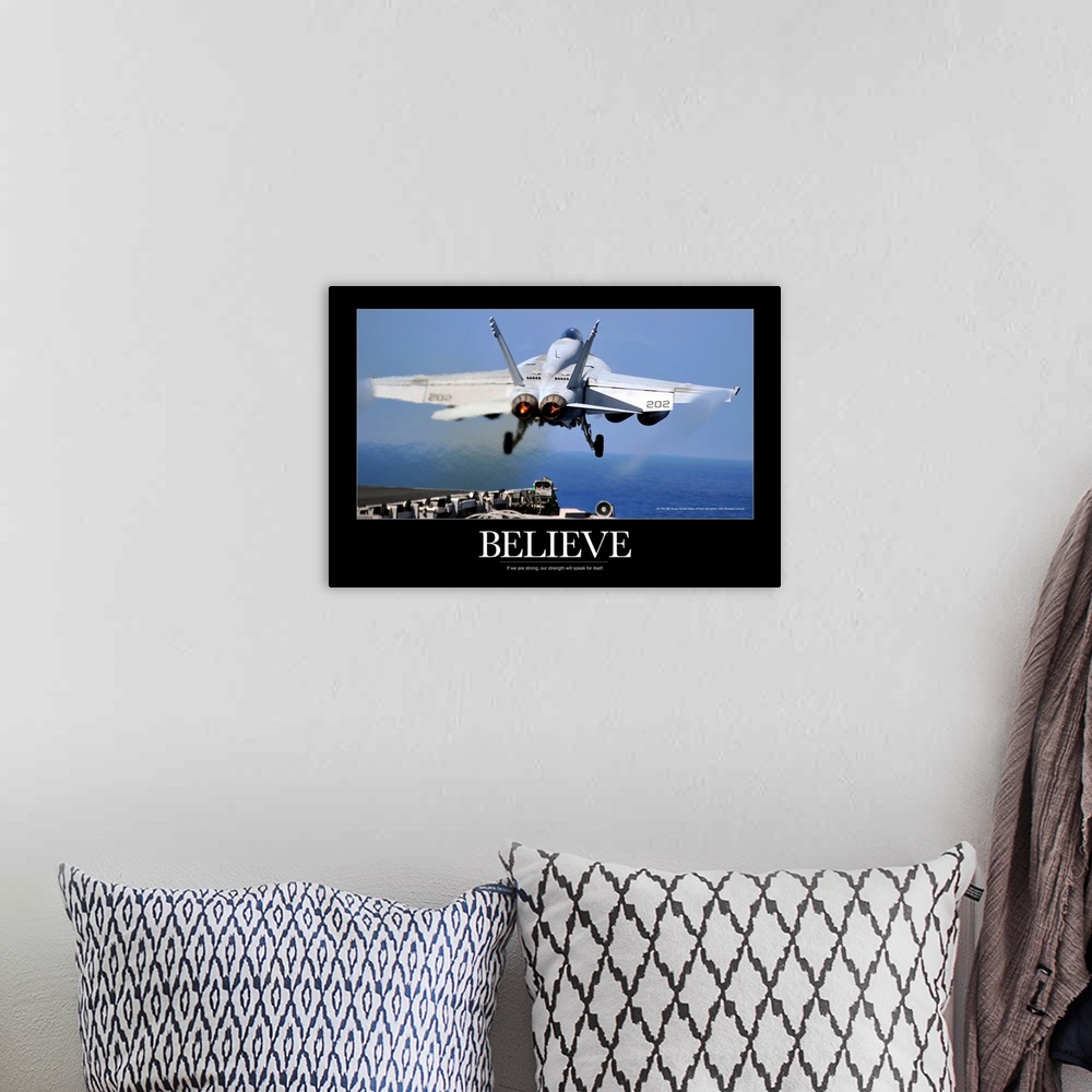 A bohemian room featuring Large poster of a jet taking off from a ship with a black border around the picture and the word ...