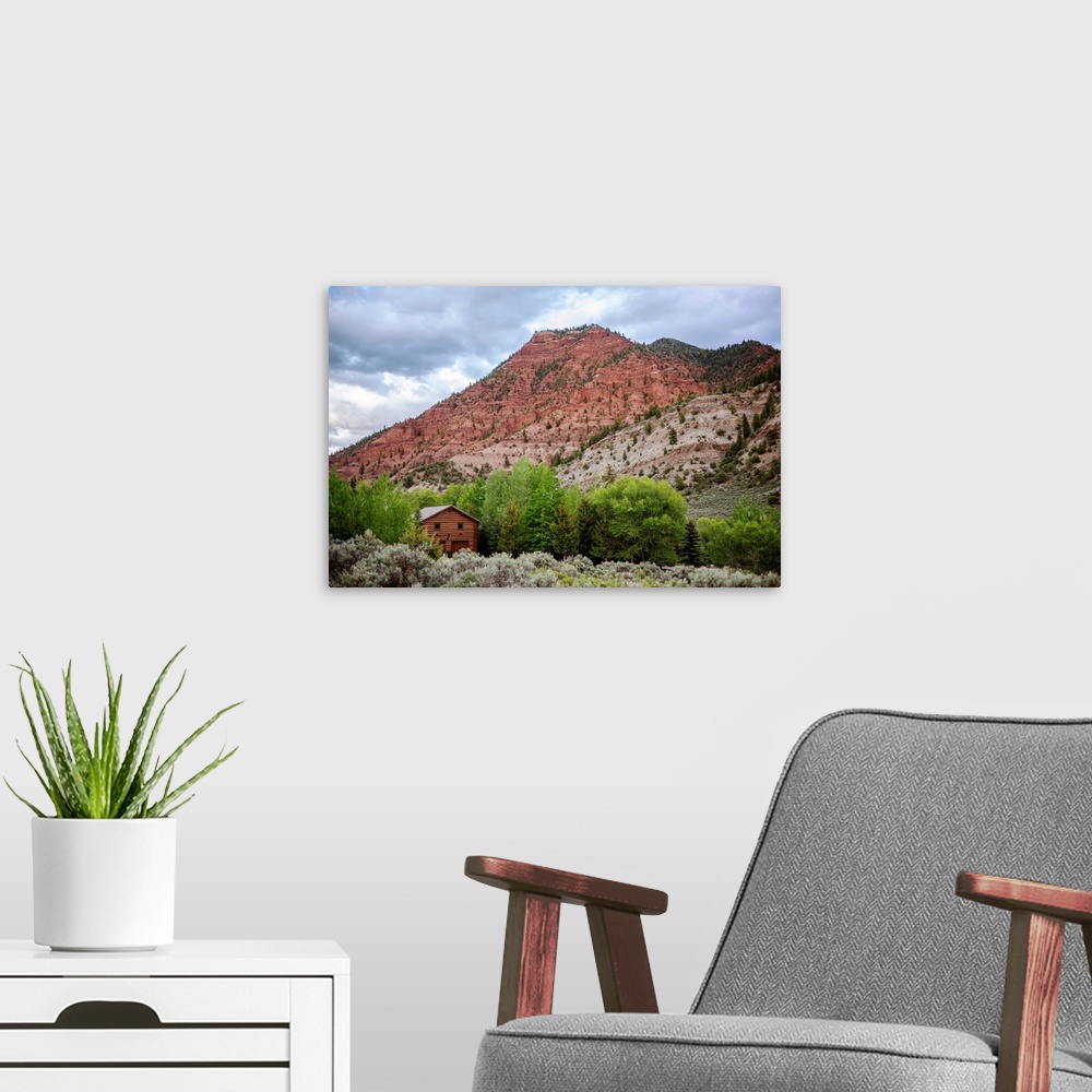 A modern room featuring Photo of a wood cabin nestled with trees under a mountain cliffside in Colorado.