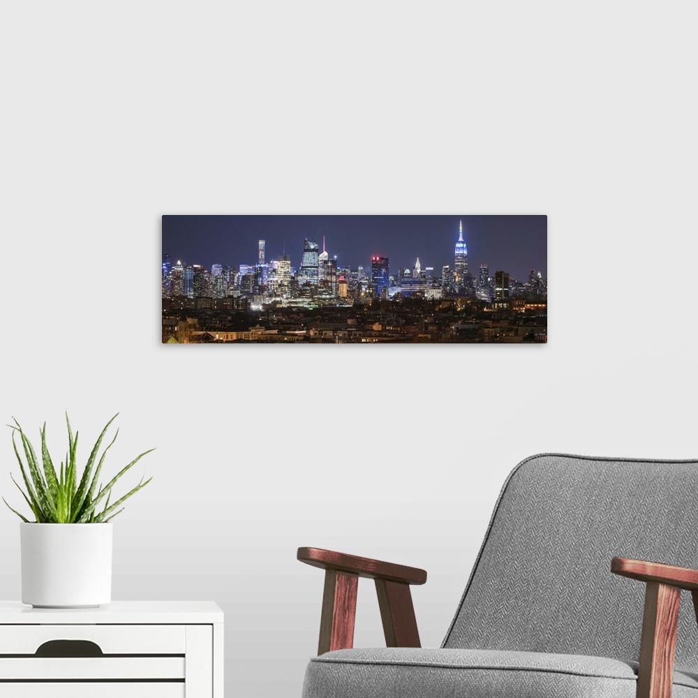 A modern room featuring Panoramic image of skyscrapers in New York City glowing at night.