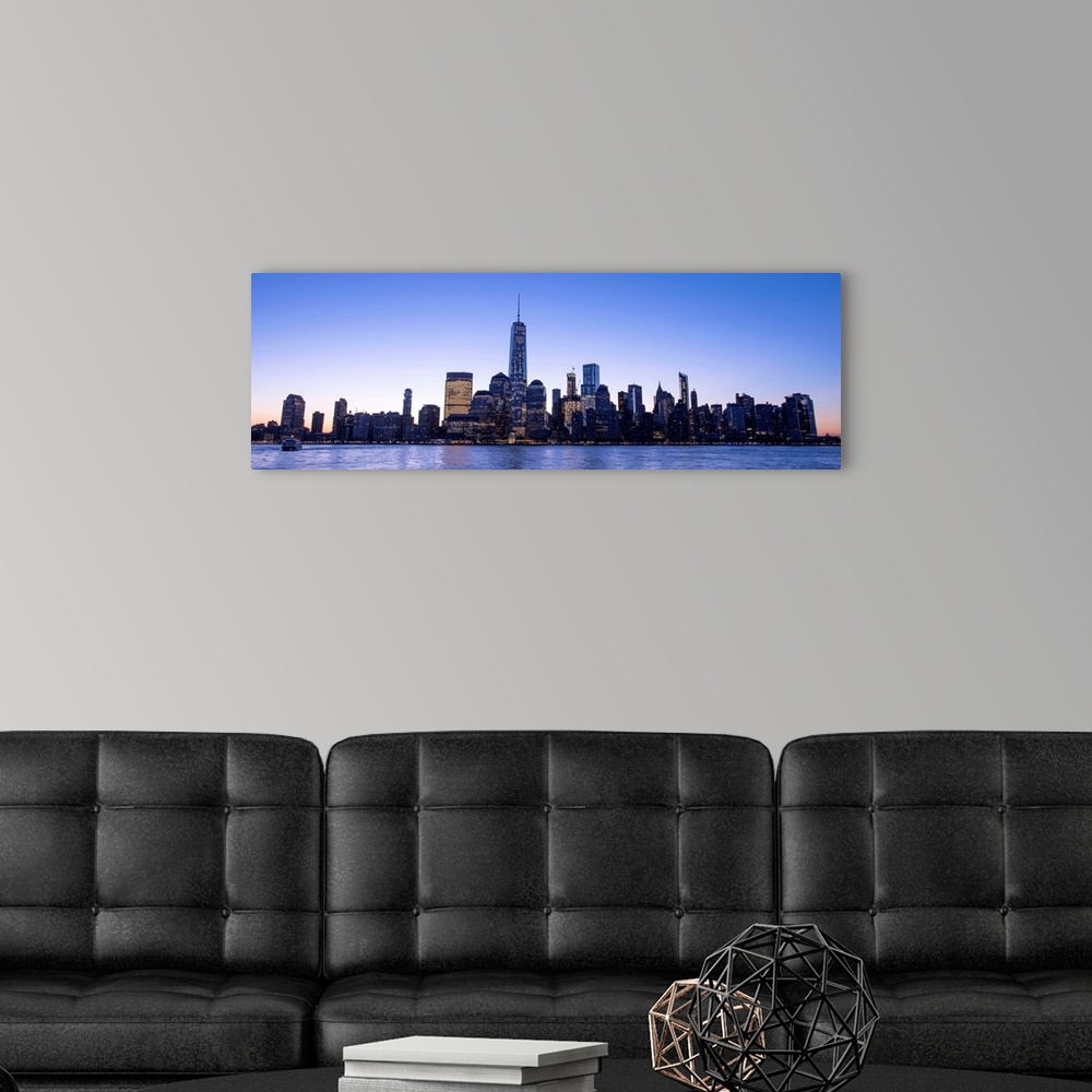 A modern room featuring Panoramic view of the New York City skyline with the One World Trade Center tower, at night.