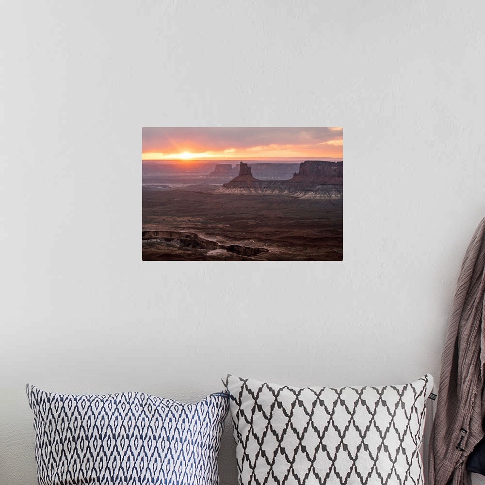A bohemian room featuring The sun setting on the horizon behind sandstone rock formations, over White Rim Trail, Canyonland...
