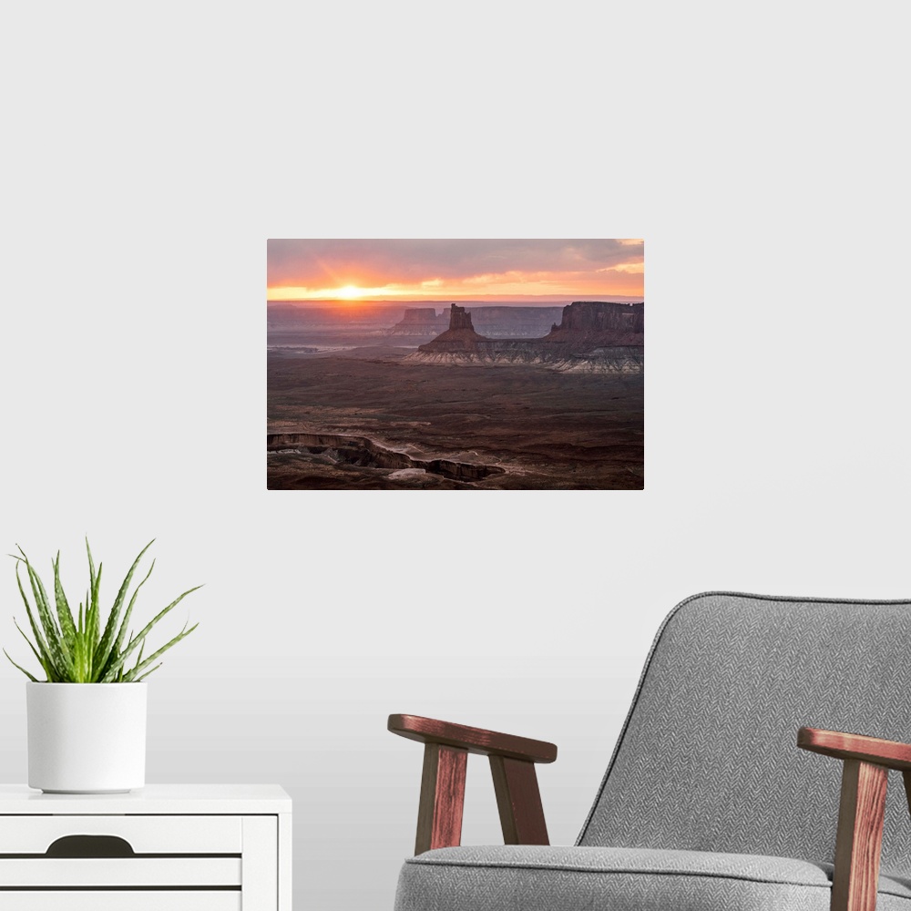 A modern room featuring The sun setting on the horizon behind sandstone rock formations, over White Rim Trail, Canyonland...