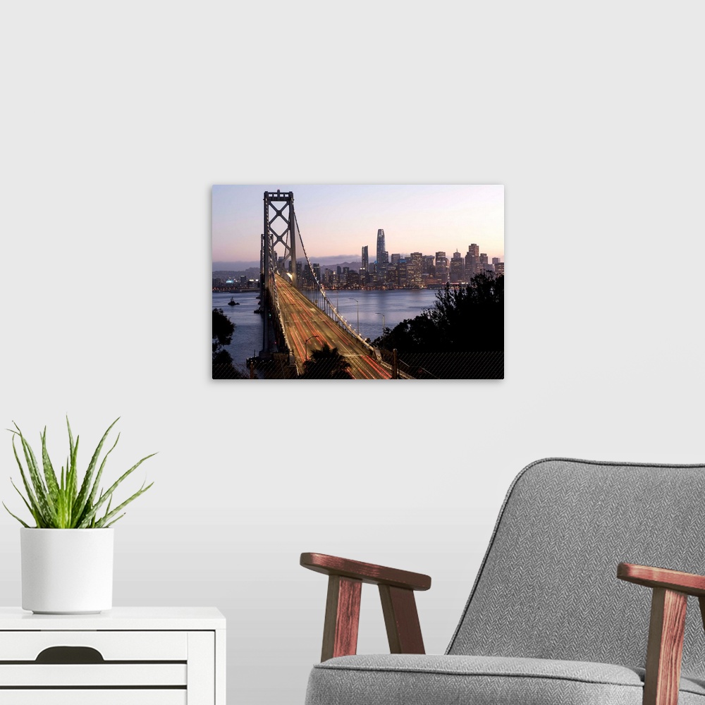 A modern room featuring Photograph of the Bay Bridge with a pink and purple sunset and the San Francisco skyline lit up i...