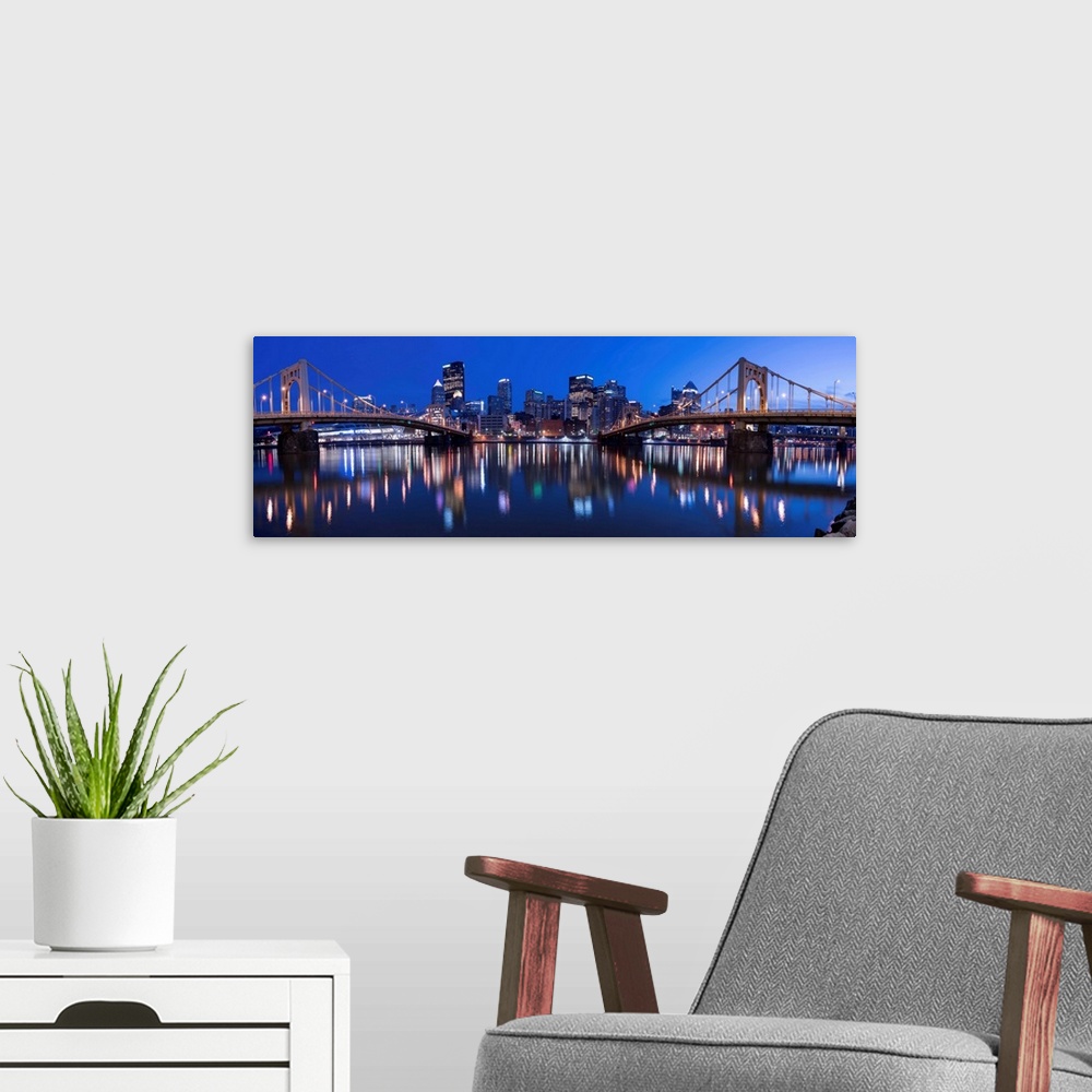 A modern room featuring Panoramic view of the Pittsburgh city skyline in the evening reflected in the water, with two of ...
