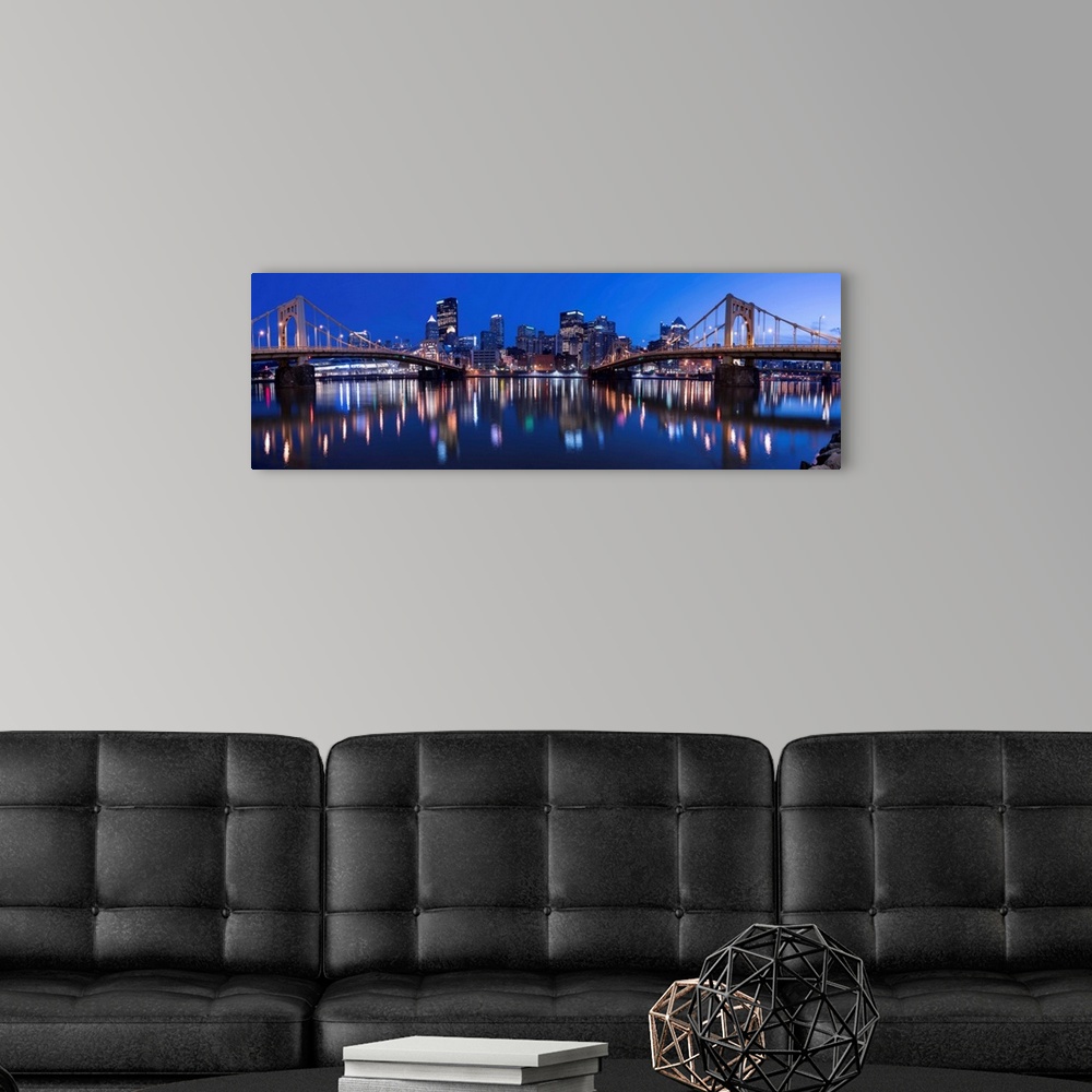 A modern room featuring Panoramic view of the Pittsburgh city skyline in the evening reflected in the water, with two of ...