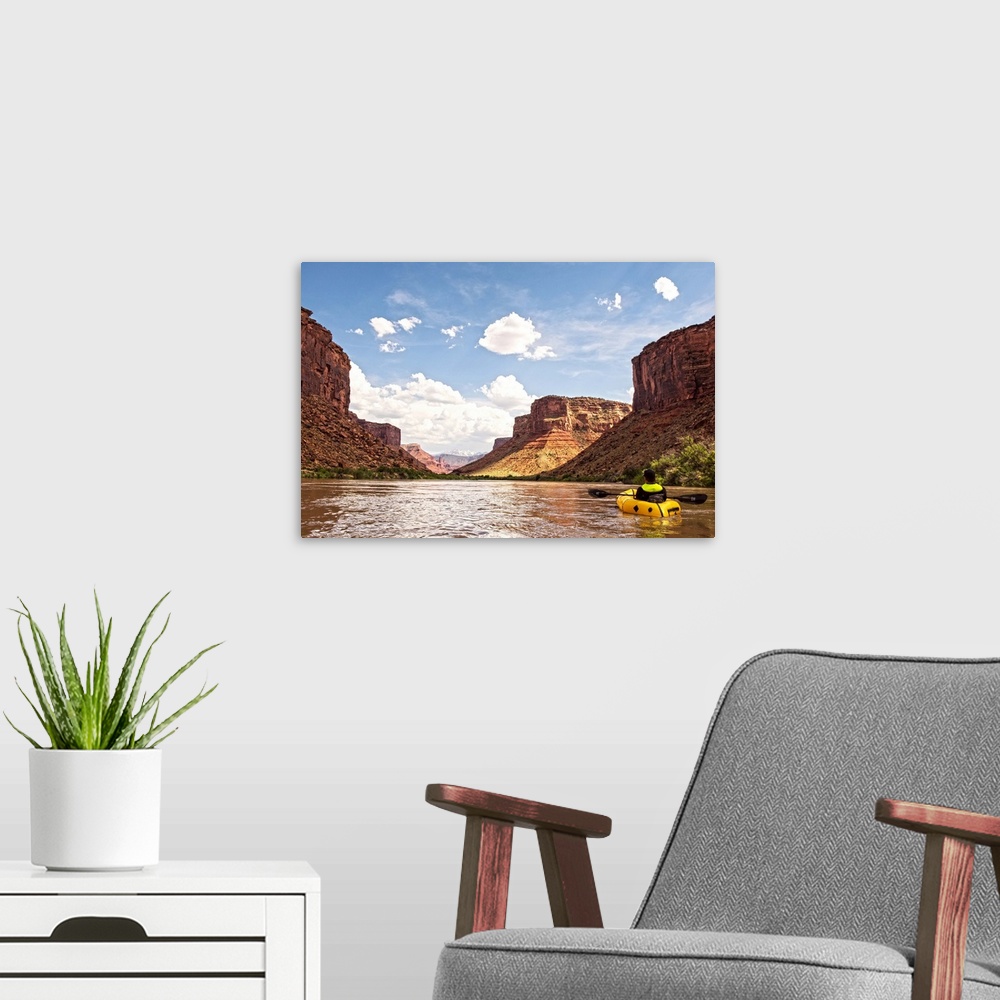 A modern room featuring Tall sandstone cliffs tower along the edge of the Colorado River, with clouds and blue skies over...