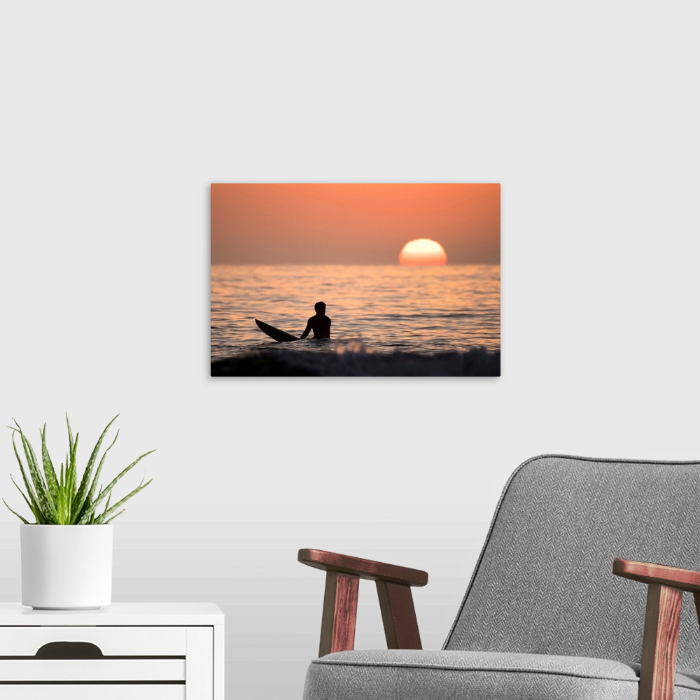 A modern room featuring Silhouetted photograph of a man sitting on his surfboard in the Pacific Ocean on the coast of San...