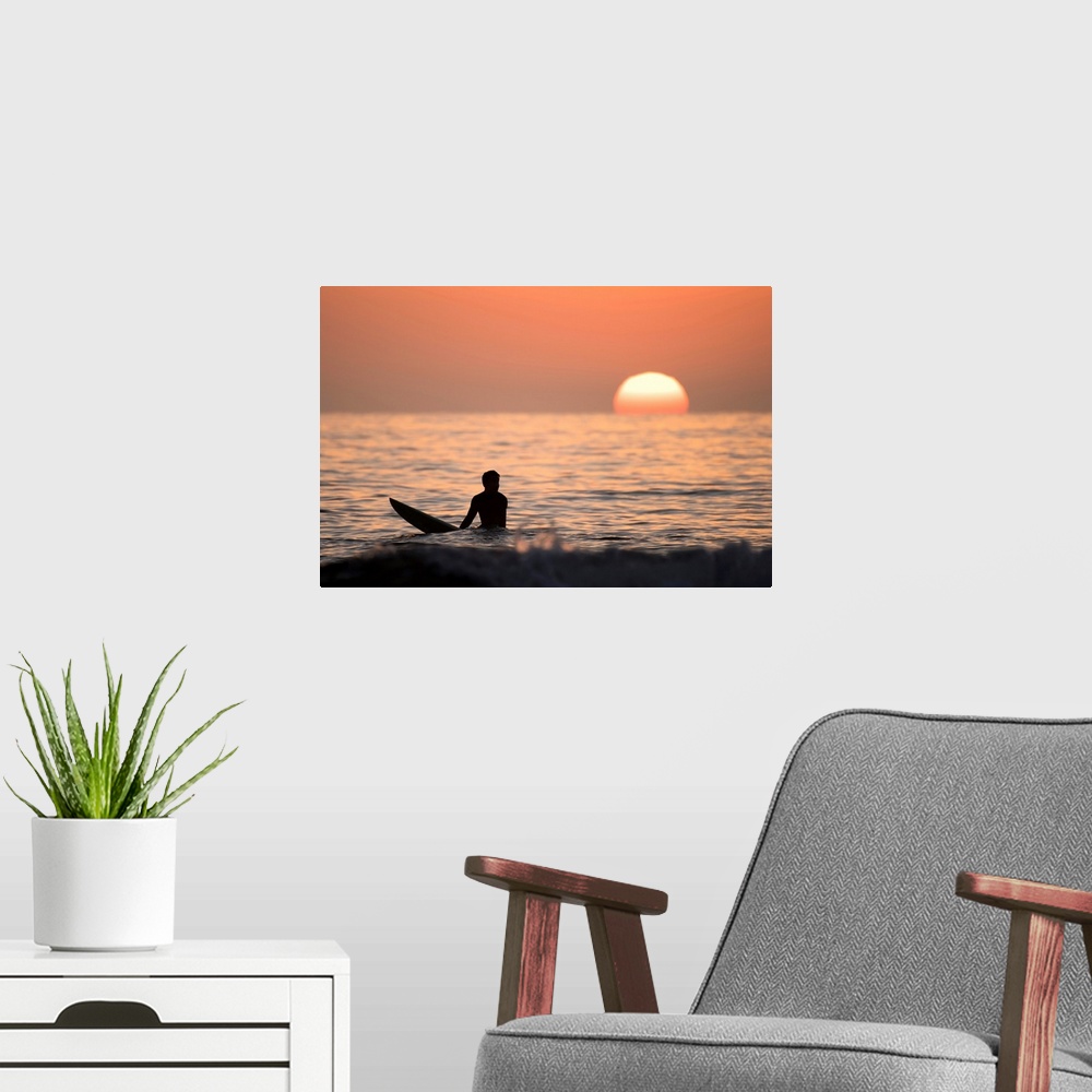 A modern room featuring Silhouetted photograph of a man sitting on his surfboard in the Pacific Ocean on the coast of San...