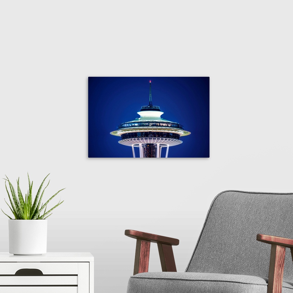 A modern room featuring Photograph of the top of the Seattle Space Needle lit up at night on a dark purple sky.