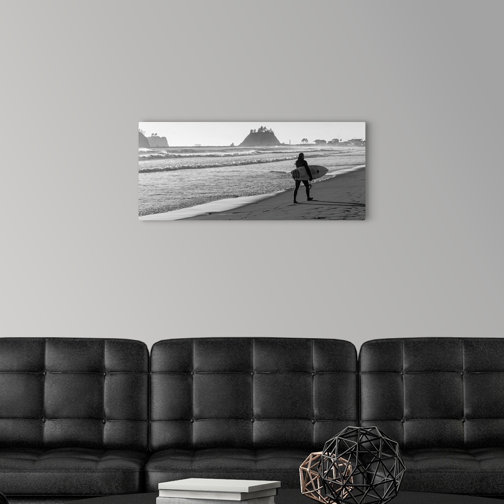 A modern room featuring Black and white panoramic photograph of a surfer walking along the shore at La Push Beach in Wash...