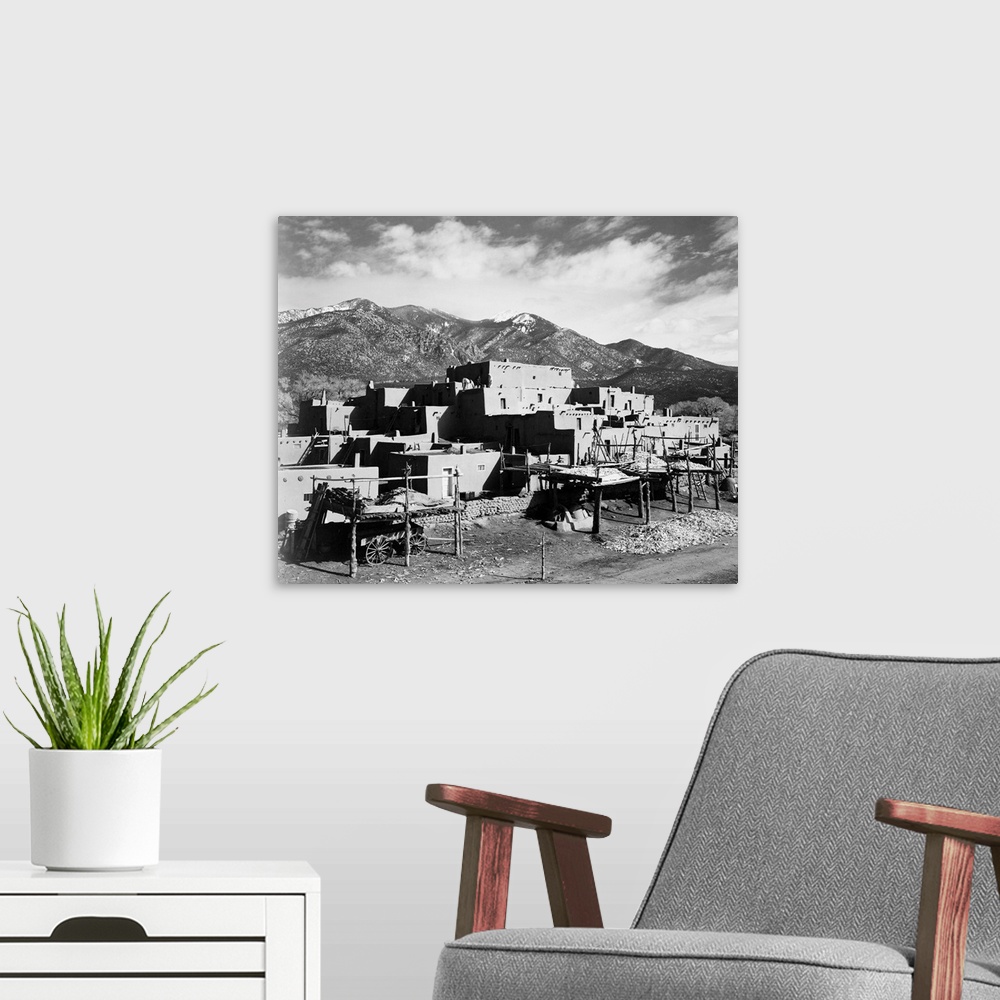 A modern room featuring Taos Pueblo, New Mexico, 1941, full view of city, mountains in background.