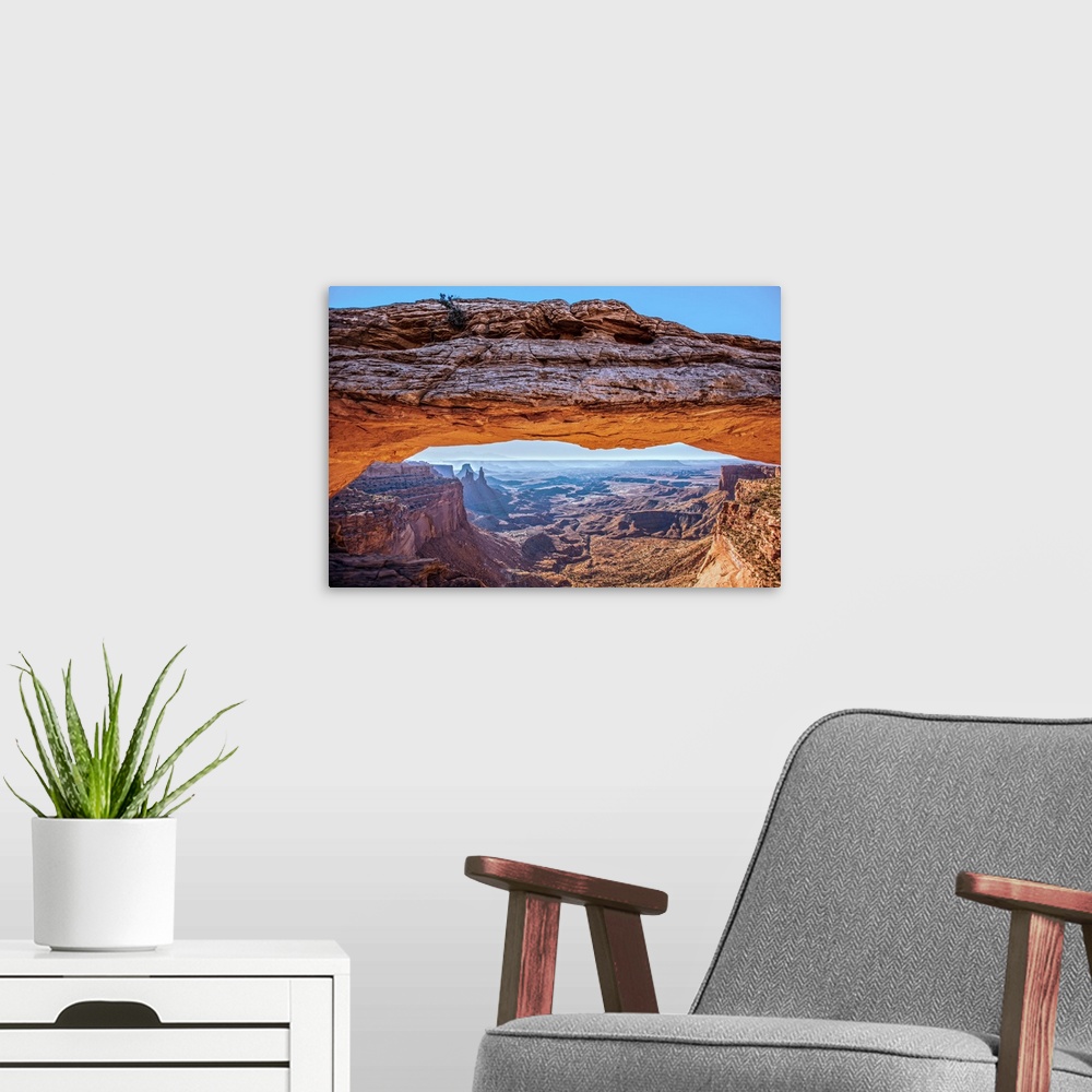 A modern room featuring The underside of the Mesa Arch glowing bright orange with sunlight, with Buck Canyon in the dista...