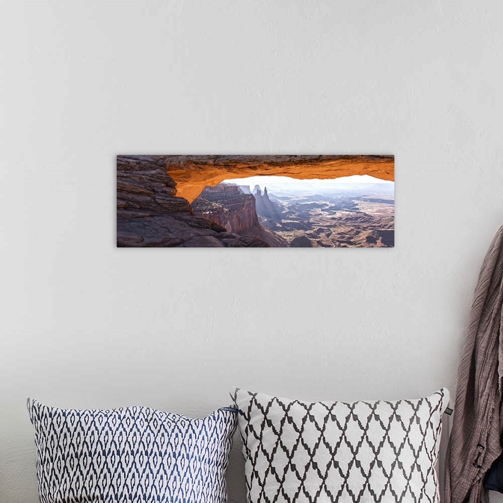A bohemian room featuring The underside of the Mesa Arch glowing bright orange with sunlight, with Buck Canyon in the dista...