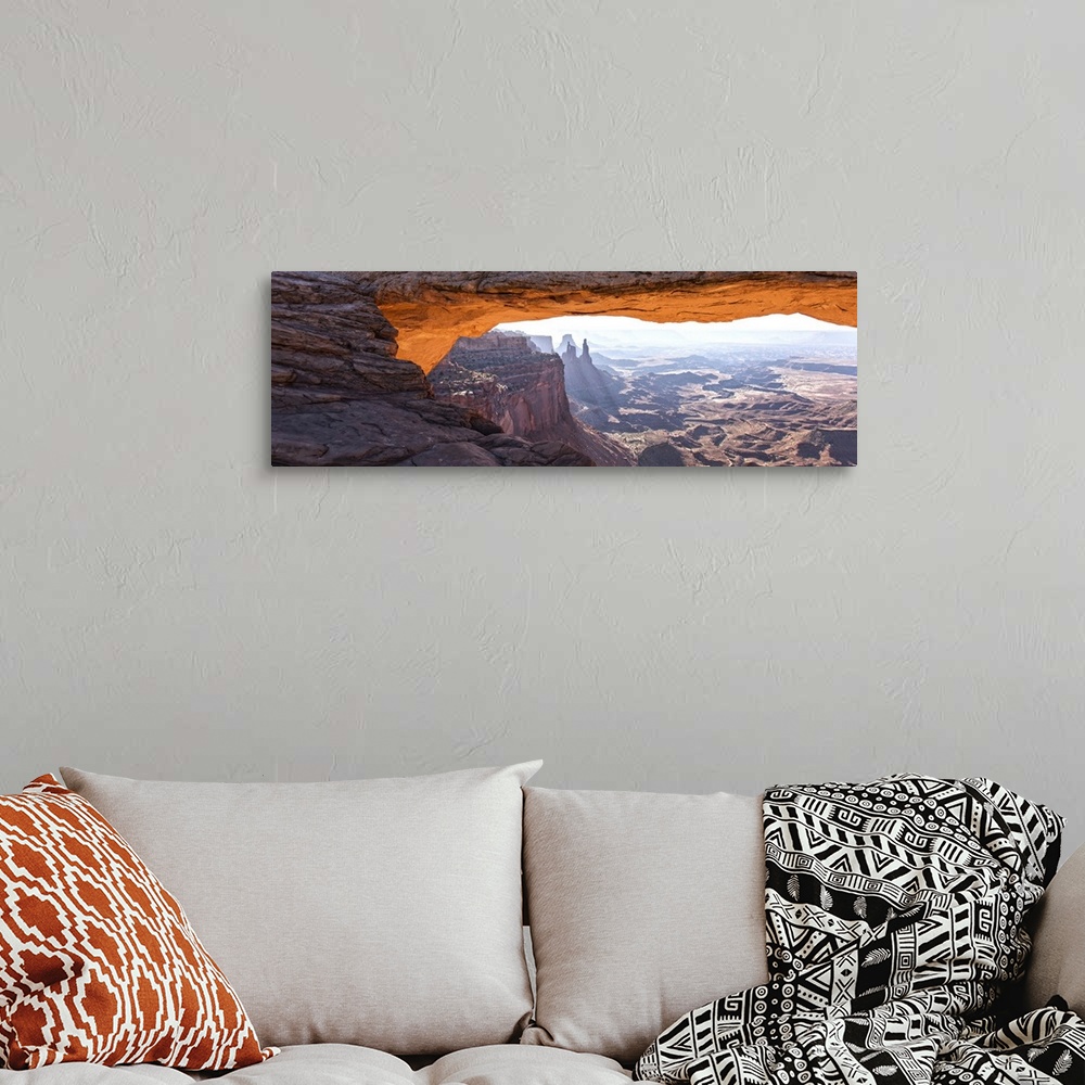 A bohemian room featuring The underside of the Mesa Arch glowing bright orange with sunlight, with Buck Canyon in the dista...
