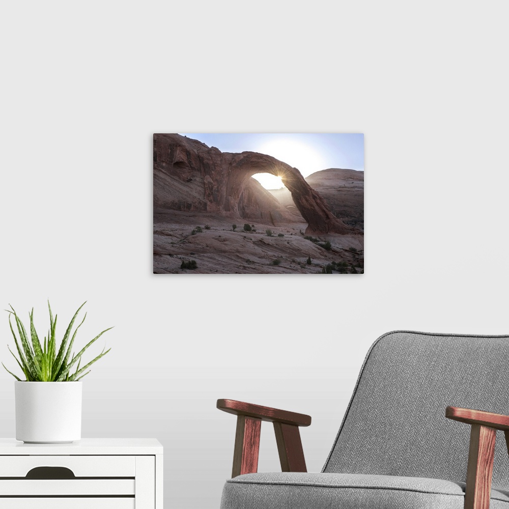 A modern room featuring The sun peeking behind the Corona Arch with a view of the desert landscape in Arches National Par...