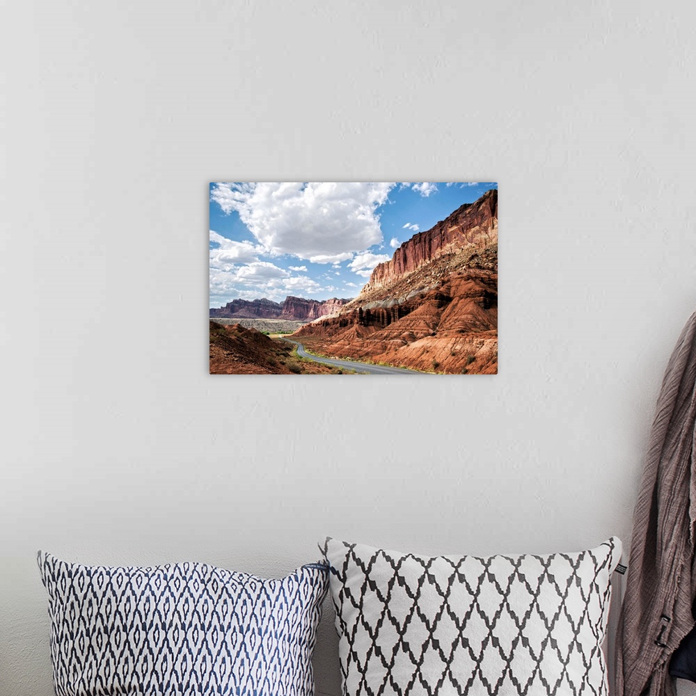 A bohemian room featuring A road winds through Capitol Reef National Park while puffy clouds scatter across a bright blue sky.