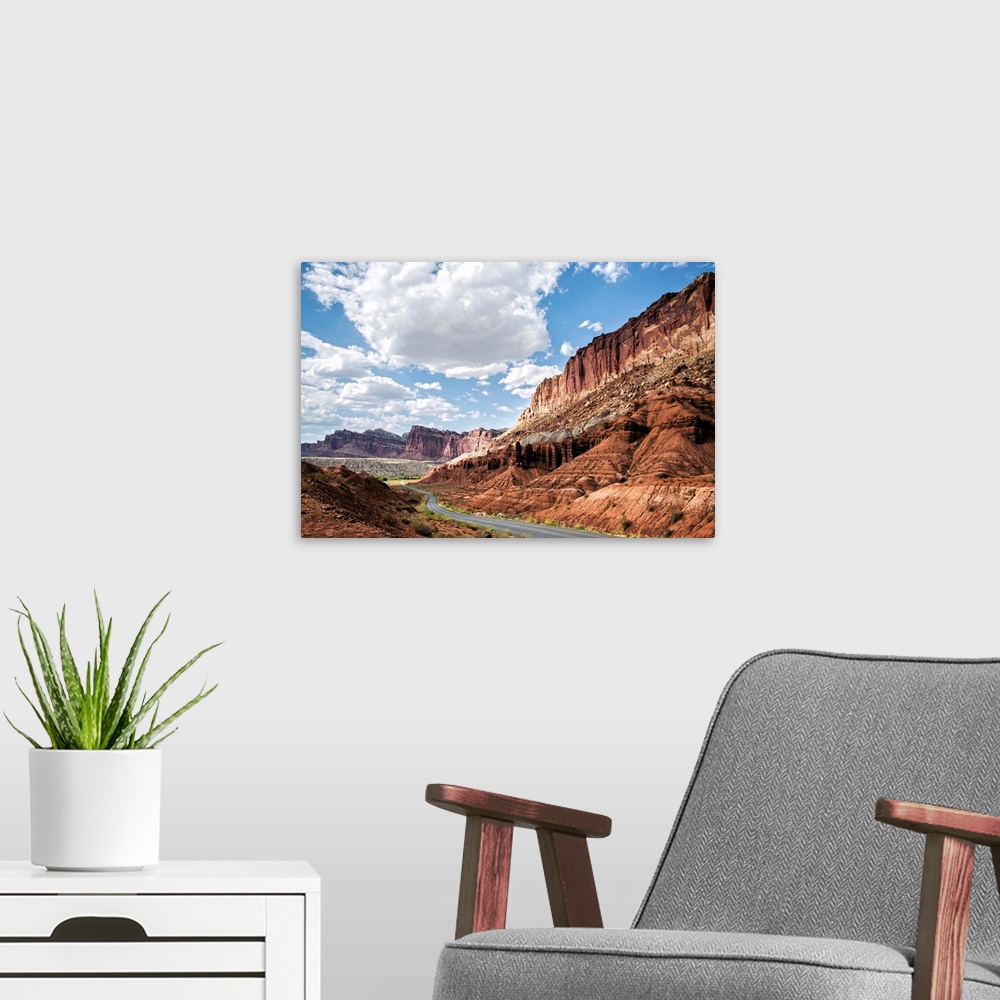 A modern room featuring A road winds through Capitol Reef National Park while puffy clouds scatter across a bright blue sky.