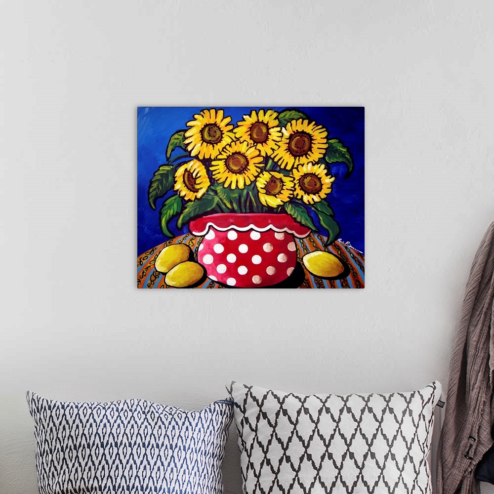 A bohemian room featuring Fun and colorful red polka dotted vase filled with sunflowers. Three lemons sit along side.