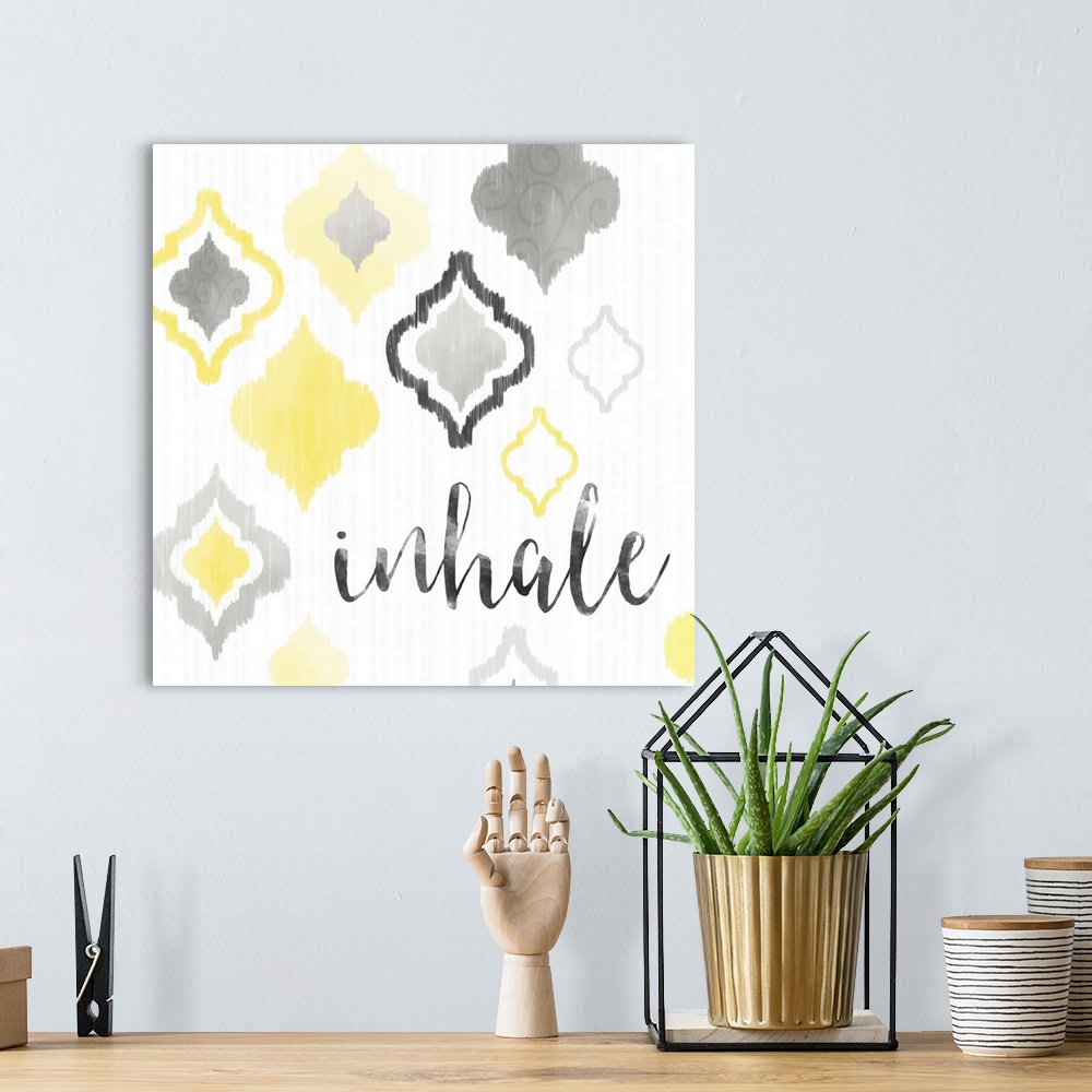 A bohemian room featuring A square decorative artwork of Moroccan tile designs in yellow and gray with the text 'inhale'.